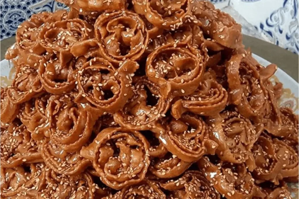 Moroccan Chebbakia pastries coated in honey and sprinkled with sesame seeds, arranged on a decorative plate.
