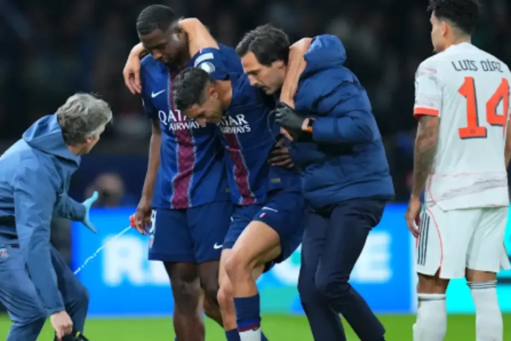 Achraf Hakimi sits on the pitch holding his leg after a muscle injury during a PSG match, as medical staff and teammates look on with concern